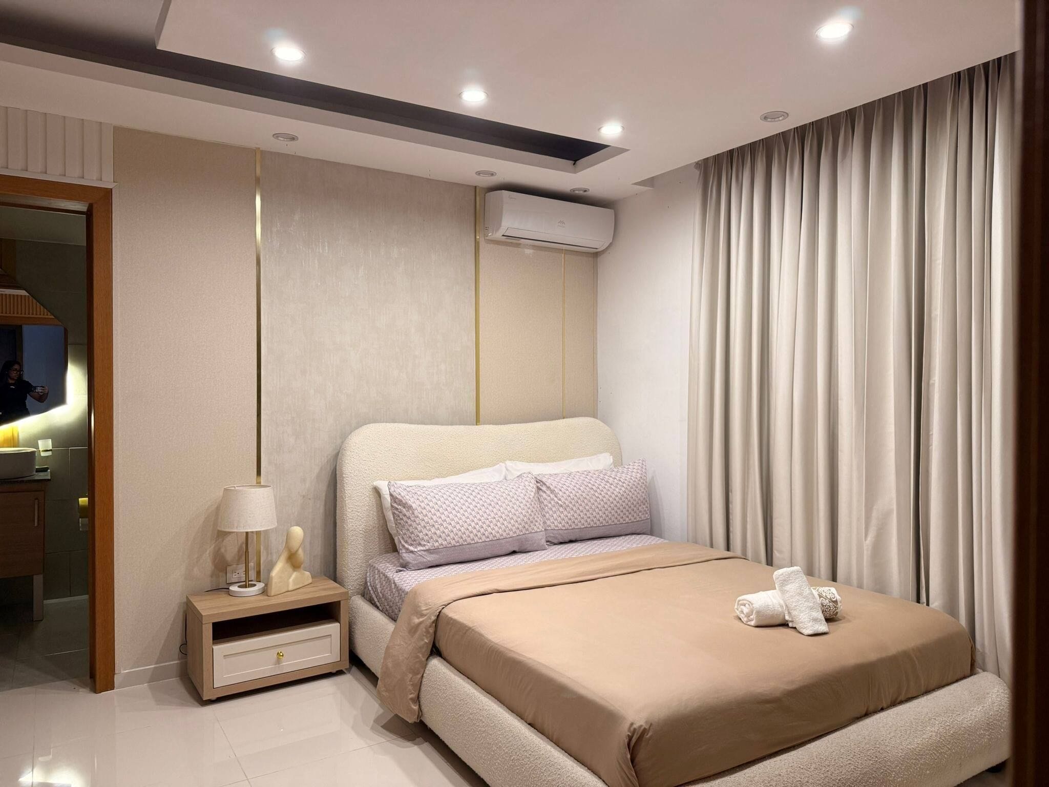 Un dormitorio moderno con cama, mesita de noche, lámpara y aire acondicionado.