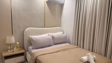 Una habitación de hotel moderna con una cama, una mesita de noche, una lámpara y un equipo de aire acondicionado.