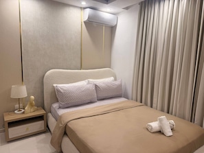 Una habitación de hotel moderna con una cama, una mesita de noche, una lámpara y un equipo de aire acondicionado.
