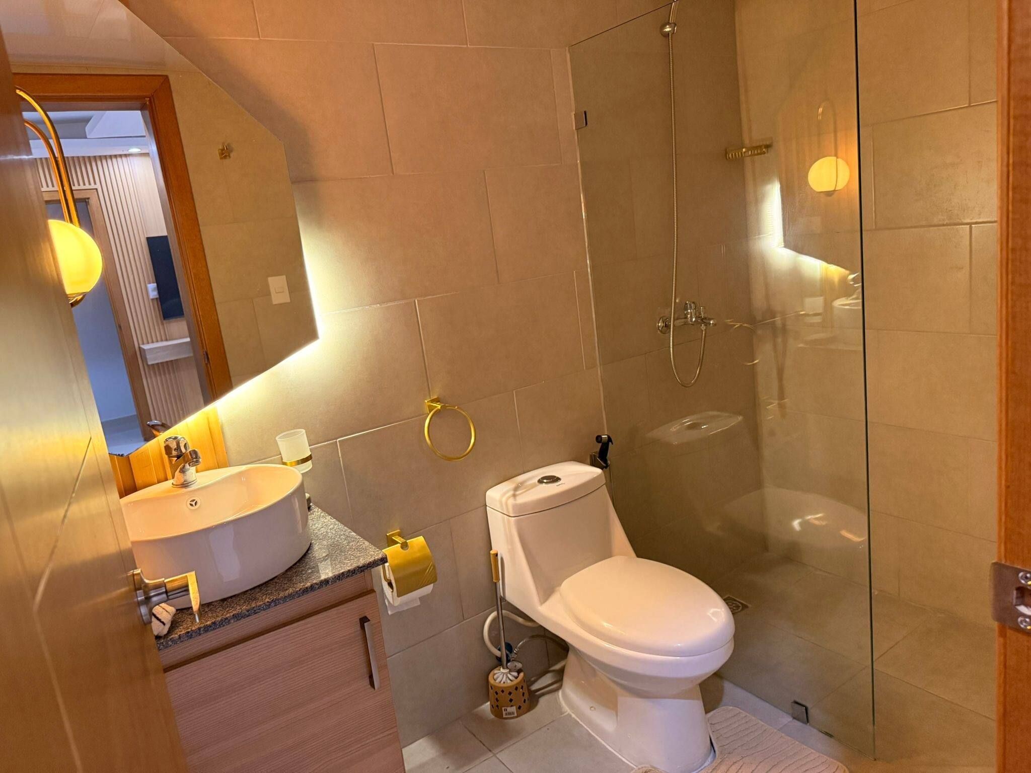 Un baño moderno con cabina de ducha de vidrio, inodoro blanco y tocador con lavamanos.