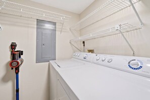 A laundry room with a front-loading washer and dryer, a hose, and two drying racks. - The Shell House • Ocean Front • Beach Access •Pool (St. Augustine)