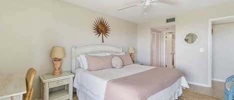 Une chambre à coucher comprenant un lit, des tables de chevet, un ventilateur de plafond, un élément de décoration murale et une porte donnant sur une autre pièce.