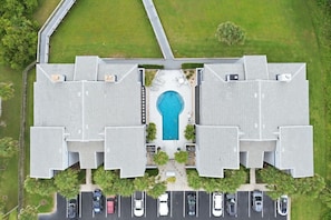 A multi-story building with a central swimming pool, parking lot, and surrounding greenery. - The Shell House • Ocean Front • Beach Access •Pool (St. Augustine)
