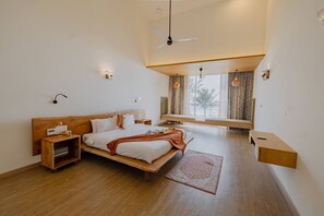 A modern bedroom with a wooden bed, bedside tables, a bench, and a view of palm trees through the window.