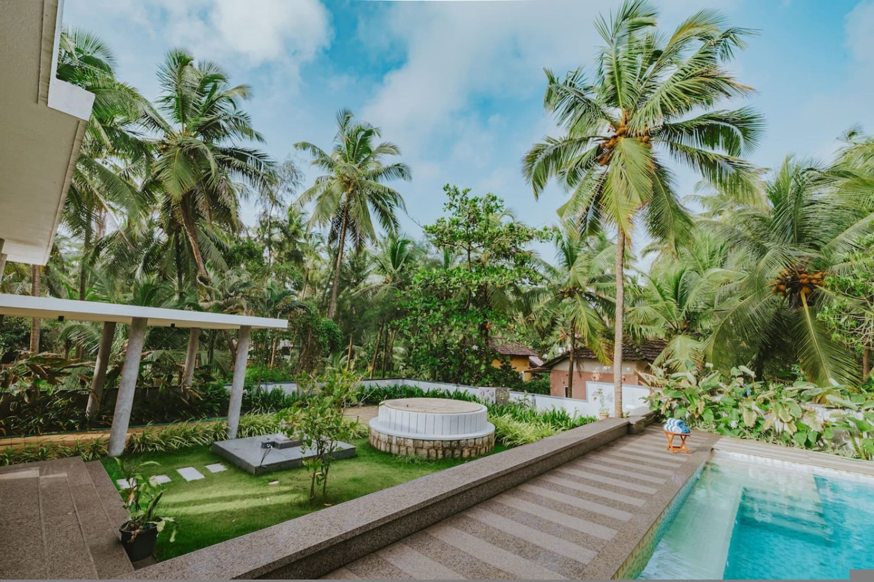 Zona junto a la piscina con un jacuzzi circular, palmeras y cielo despejado.