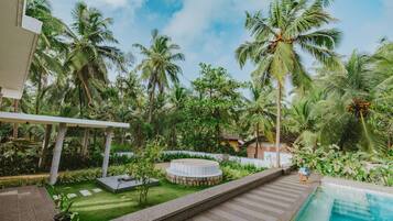 Zona junto a la piscina con un jacuzzi circular, palmeras y cielo despejado.