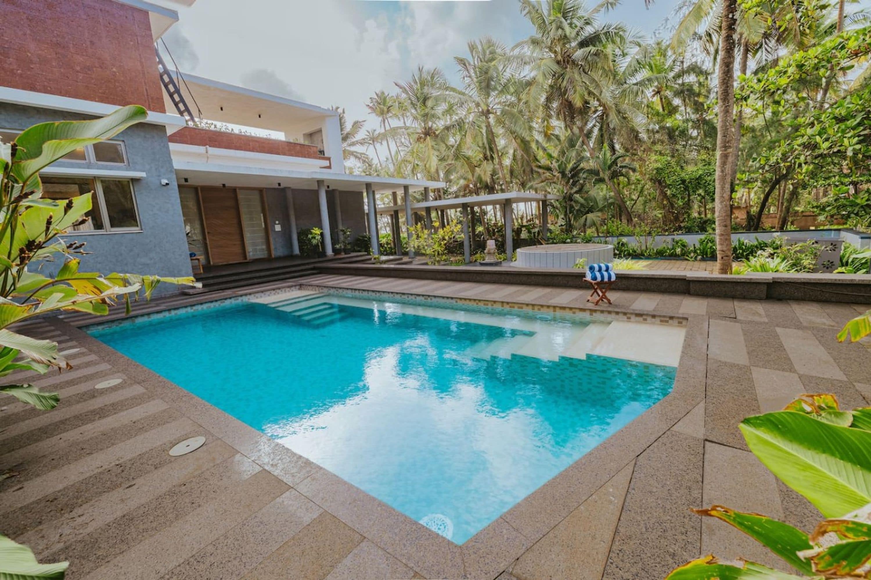 Una piscina con superficie de agua azul cristalina, rodeada por un solárium empedrado y abundante vegetación.