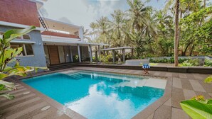 A swimming pool with a clear blue water surface, surrounded by a paved deck and lush greenery. - Villa Shankari - Beachside 3BR w Private Pool (Udupi)