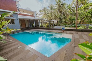 A swimming pool with a clear blue water surface, surrounded by a paved deck and lush greenery. - Villa Shankari - Beachside 3BR w Private Pool (Udupi)