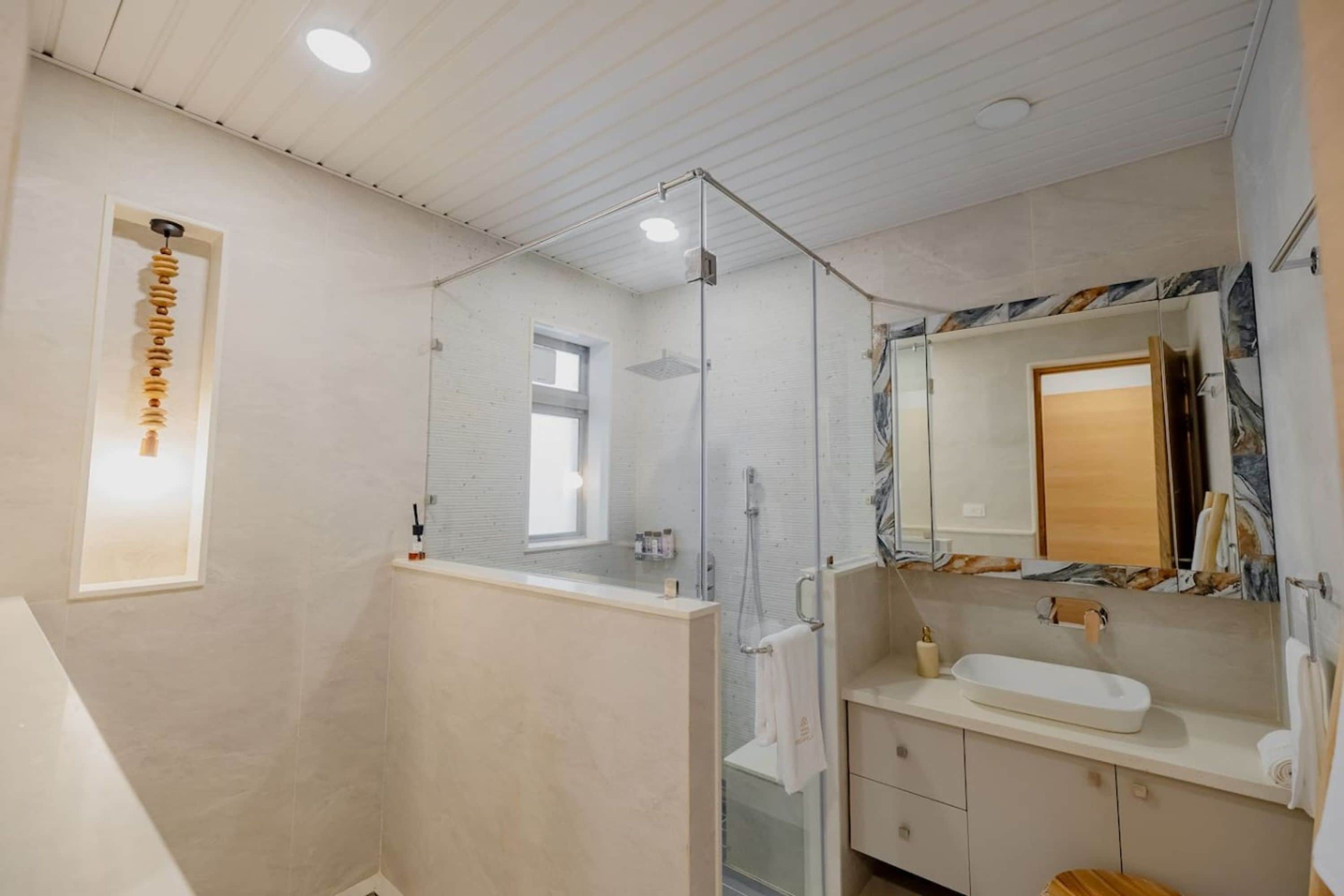 Un baño moderno con cabina de ducha de vidrio, tocador con encimera de mármol y un espejo grande con marco de madera.