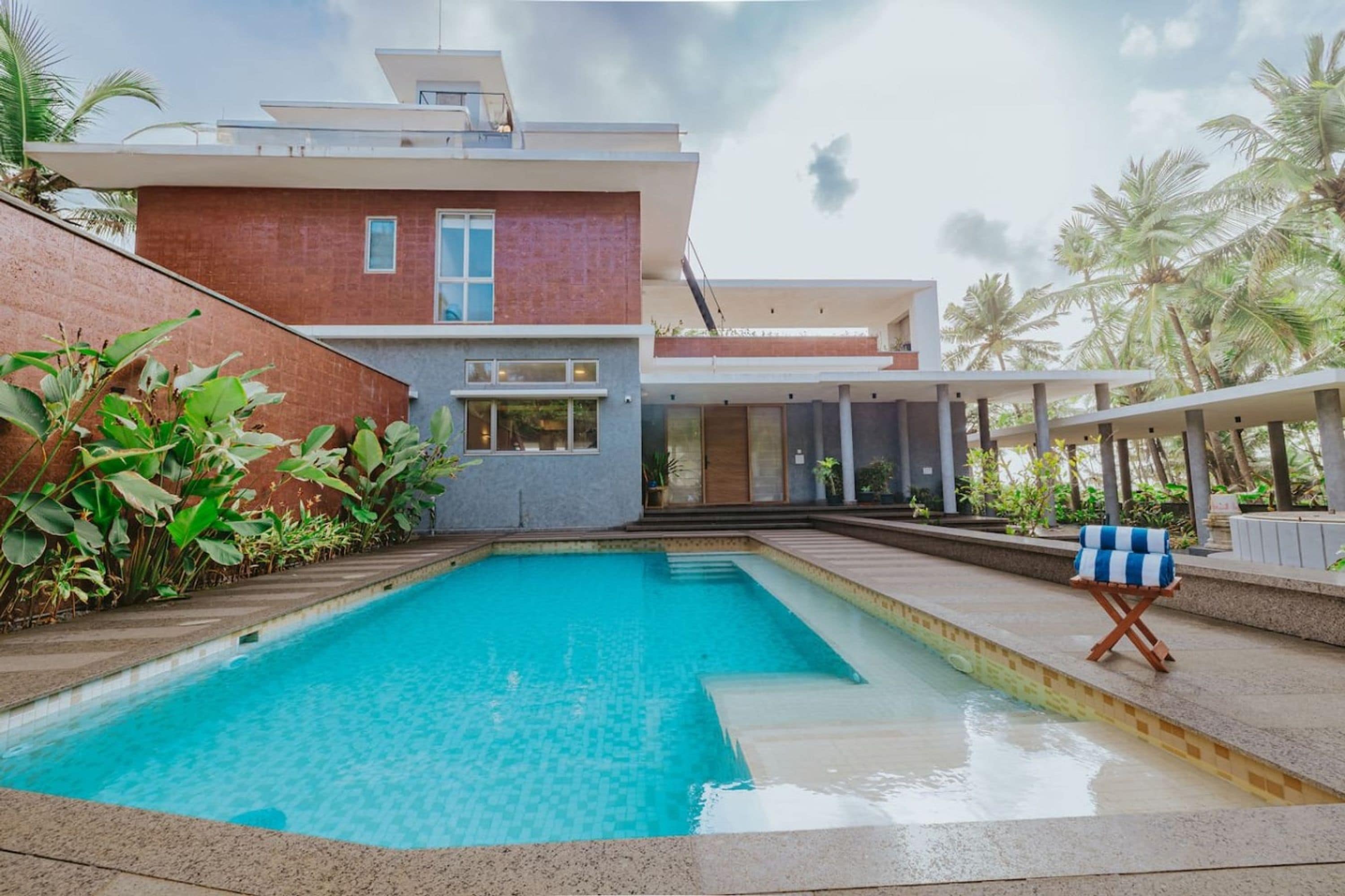 Una casa moderna con piscina, un porche cubierto y vistas a palmeras.