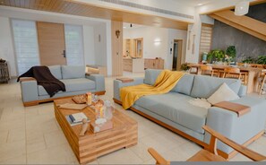 A modern living room with a sofa, coffee table, and a dining area with a table and chairs. - Villa Shankari - Beachside 3BR w Private Pool (Udupi)