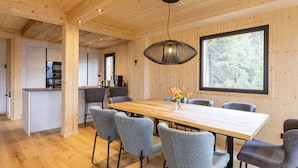 A modern interior with a wooden dining table, grey upholstered chairs, a hanging light fixture, and a large window offering a view of trees. - Superior Chalet # 27 With Sauna & Hot Tub (Stadl-Predlitz)