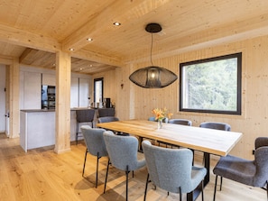 A modern interior with a wooden dining table, grey upholstered chairs, a hanging light fixture, and a large window offering a view of trees. - Superior Chalet # 27 With Sauna & Hot Tub (Stadl-Predlitz)