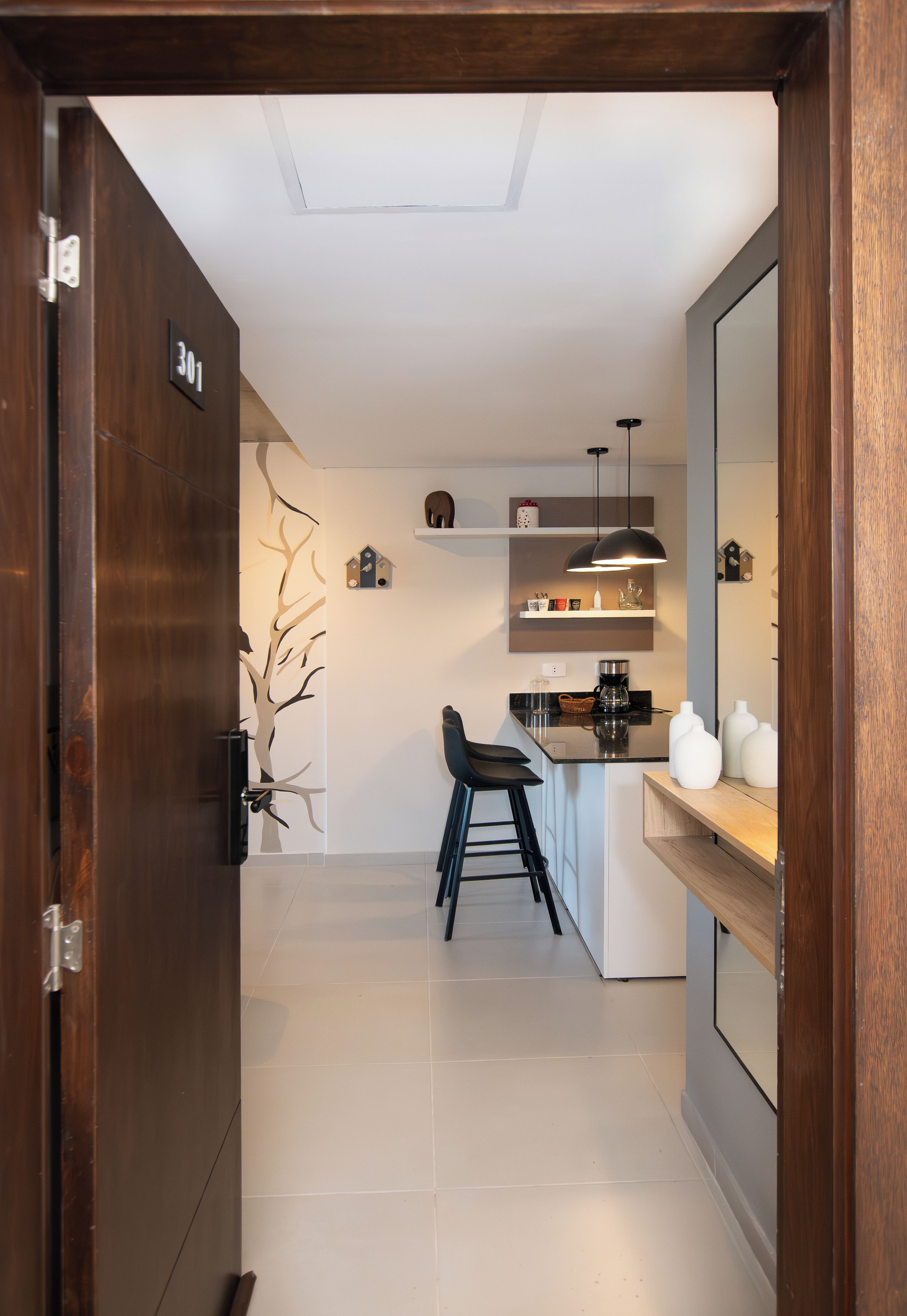 Una cocina moderna con puerta de madera, pared blanca con un adhesivo de árbol, una silla negra y una cafetera.
