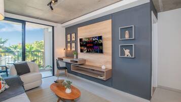 Uma sala de estar moderna com uma grande televisão de tela plana na parede, um sofá, uma mesa de centro e uma varanda com vista para palmeiras.