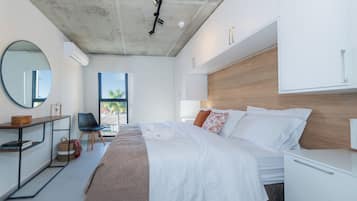 A modern bedroom with a large bed, a bedside table, a mirror, and a view of the outdoors.
