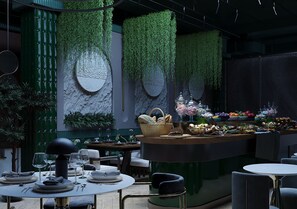 An indoor dining area with round tables, chairs, and a central bar with food and drink displays.