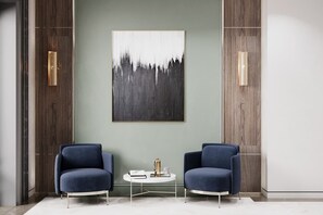 A modern room with two blue armchairs, a white coffee table, and a large abstract painting on the wall.