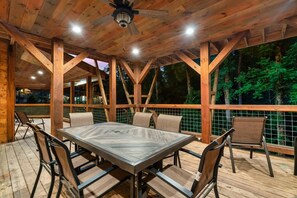 An outdoor wooden deck with a table and chairs, surrounded by a wooden railing. - Luxury4bdrmCabin-LgPool-HotTub-5MinParkway-Special (Sevierville)