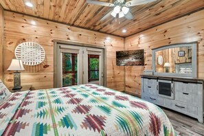 A wooden-paneled bedroom with a bed, a dresser, a round wall clock, and a television. - Luxury4bdrmCabin-LgPool-HotTub-5MinParkway-Special (Sevierville)
