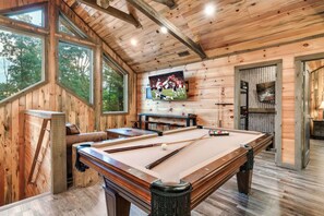 A wooden interior with a pool table, a television mounted on the wall, and large windows. - Luxury4bdrmCabin-LgPool-HotTub-5MinParkway-Special (Sevierville)