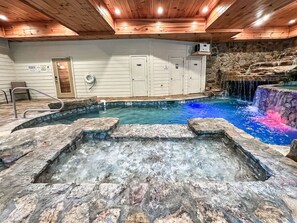 A hot tub area with a stone basin, a pool with a waterfall feature, and a stone wall. - Luxury4bdrmCabin-LgPool-HotTub-5MinParkway-Special (Sevierville)
