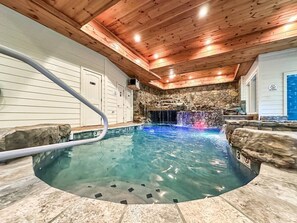 Une piscine intérieure avec un mur en pierre en arrière-plan, un plafond en bois et une eau cristalline.