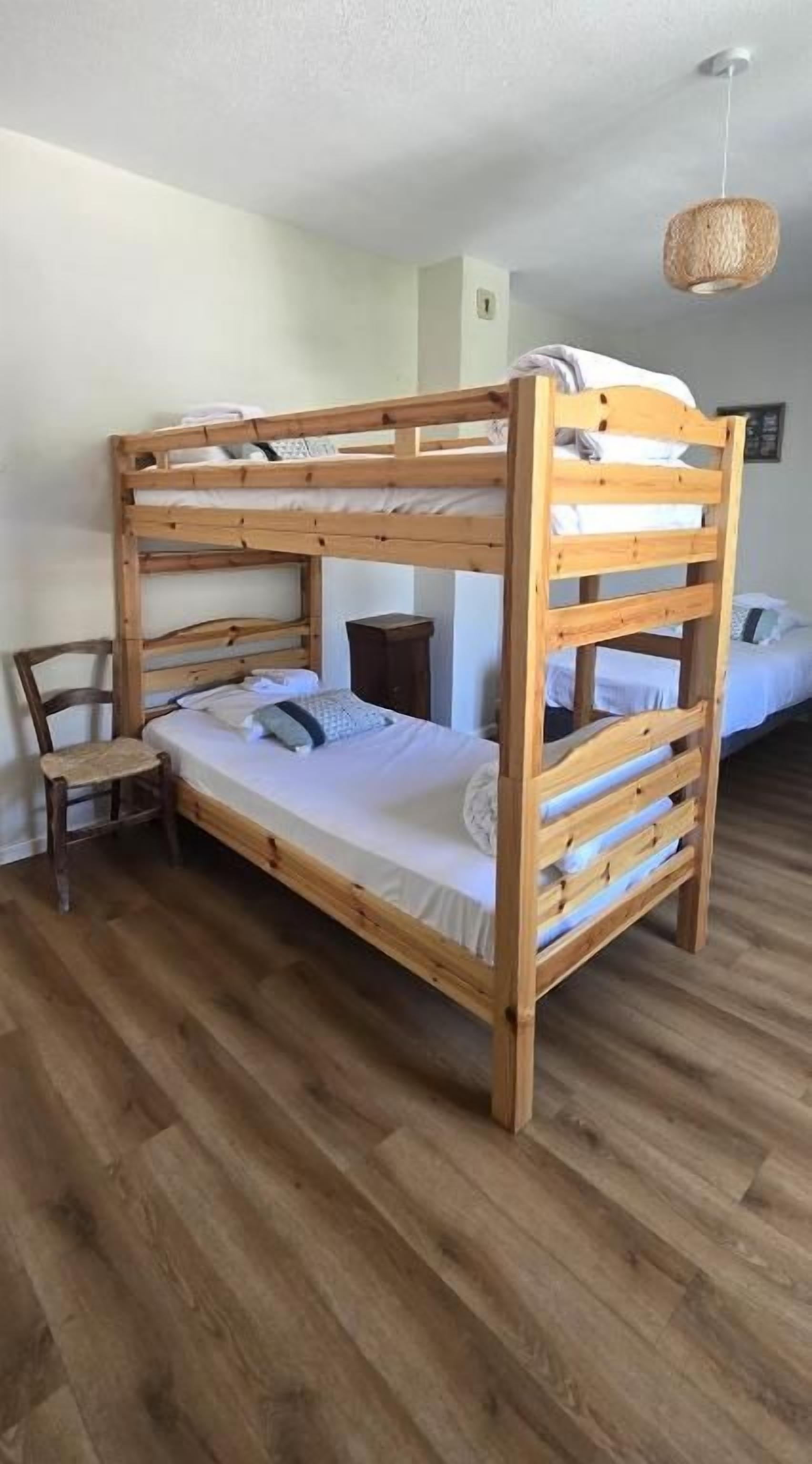 A bunk bed with a wooden frame, a small bedside table, and a chair.