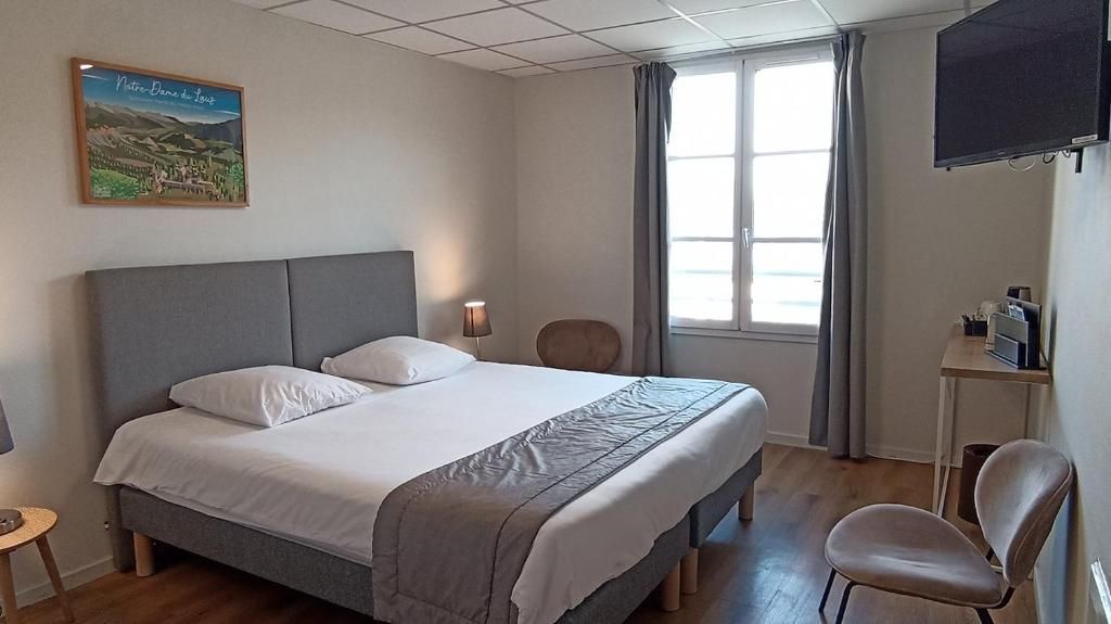 A hotel room with a large bed, a desk, a chair, a television, and a window with curtains.