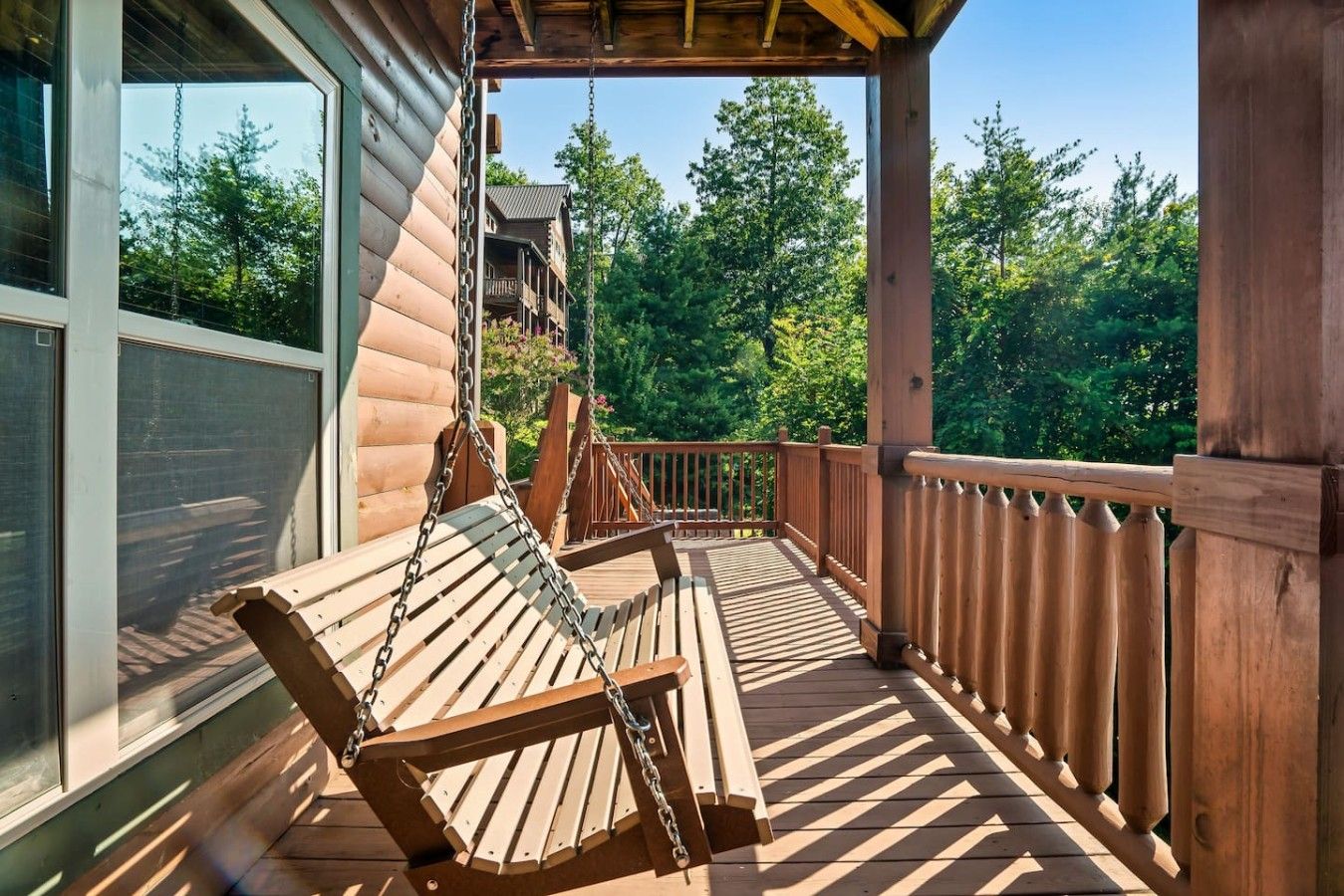 Une terrasse en bois avec une chaise suspendue, une balustrade et une vue sur une zone boisée.