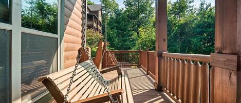 Une terrasse en bois avec une chaise suspendue, une balustrade et une vue sur une zone boisée.