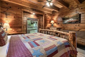 A log cabin bedroom with a bed, a window, a lamp, and a painting on the wall. - Indoor Golf Cabin Amazing Views Arcade 8BRDM Cabin (Sevierville)