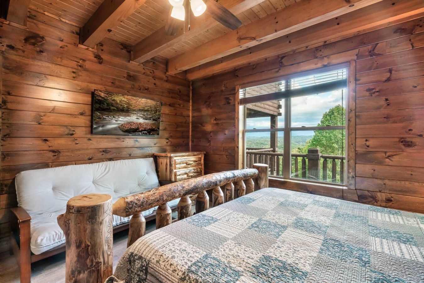 A log cabin room with a bed, a white sofa, a wooden headboard, a window with a view, and a painting on the wall.