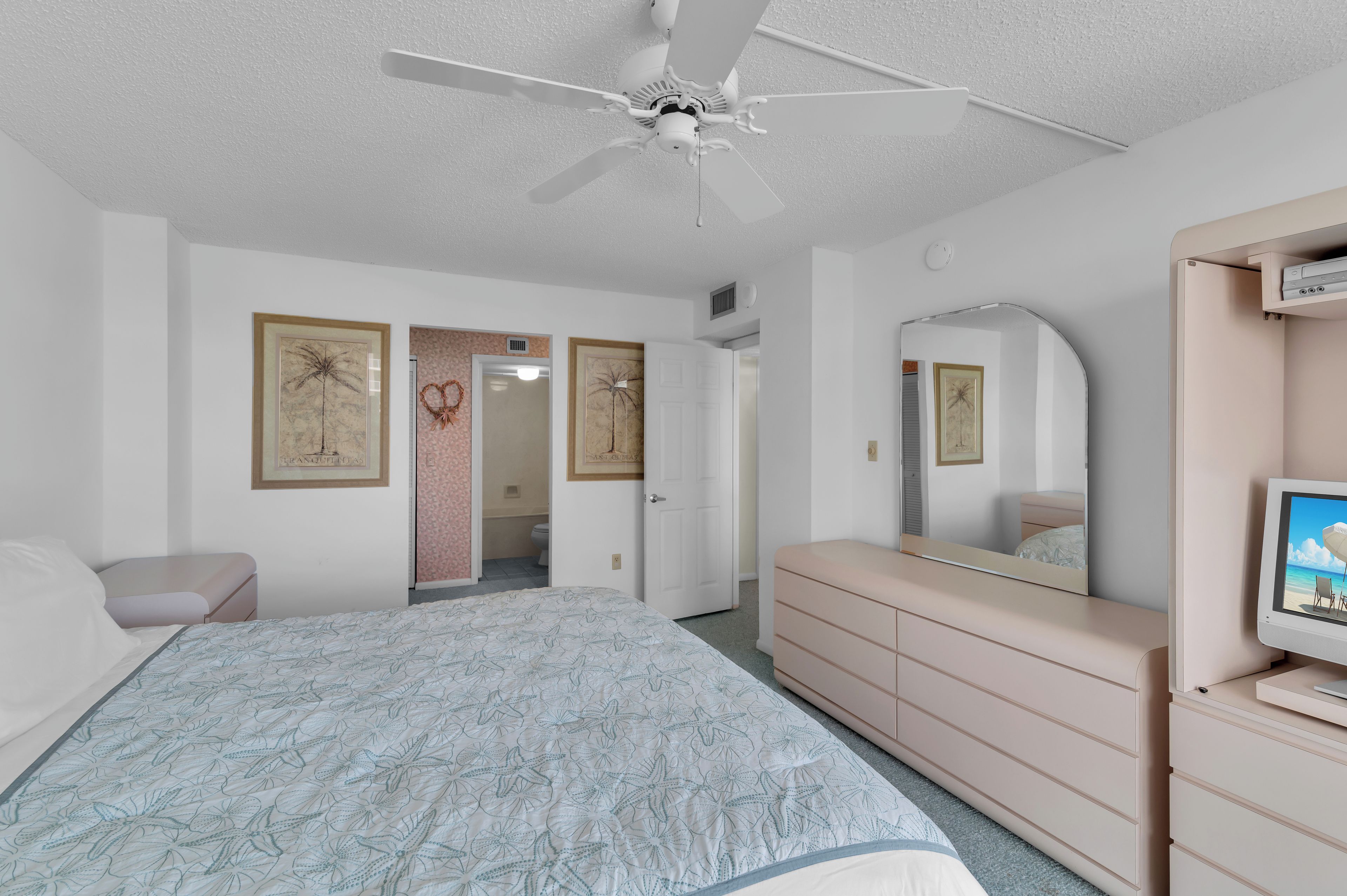 Ein Schlafzimmer mit Bett, Kommode, Deckenventilator und Fernseher.