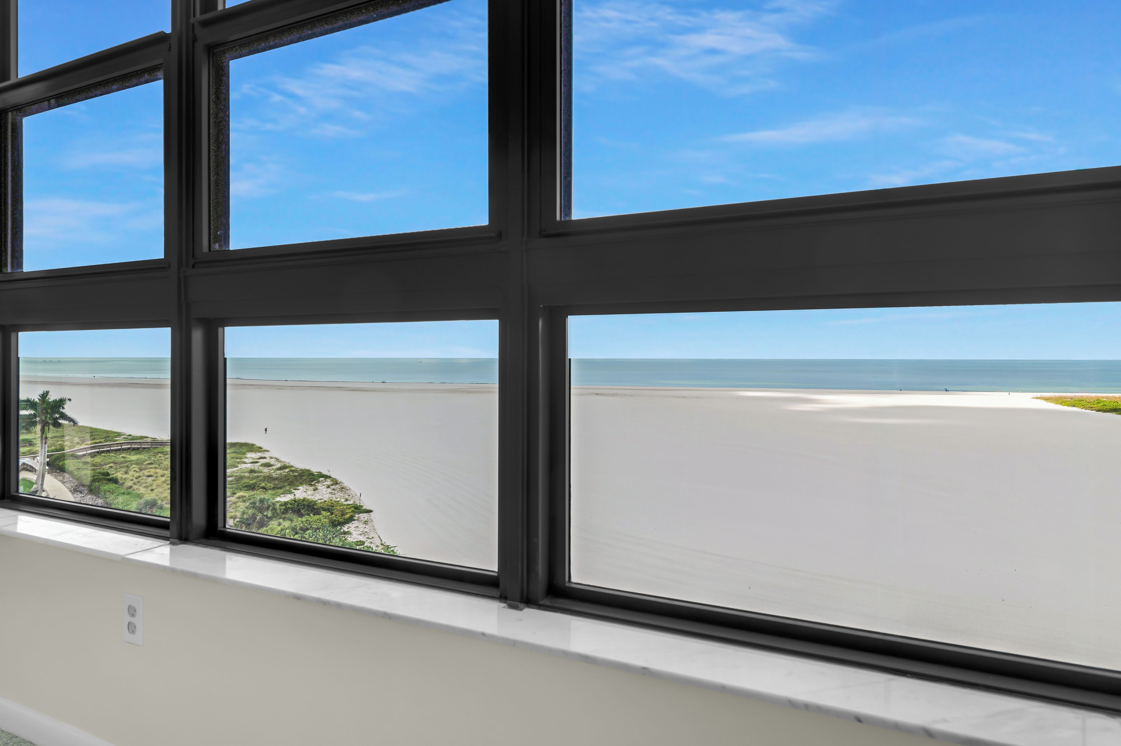A view through a window with a clear sky and a beach in the distance.