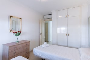 Une chambre à coucher avec une commode en bois, un lit avec du linge de lit blanc, un miroir et une armoire.
