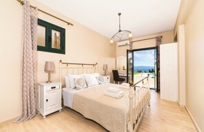 Ein Schlafzimmer mit Bett, Nachttischen, einem Sessel, einem Schreibtisch und Meerblick.