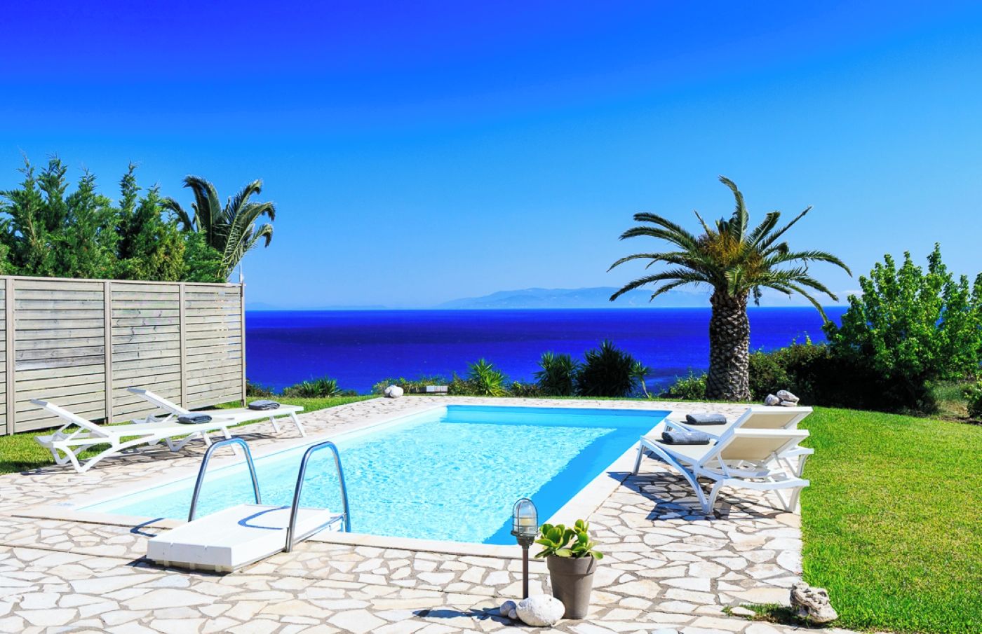 A swimming pool with lounge chairs and a view of the sea.