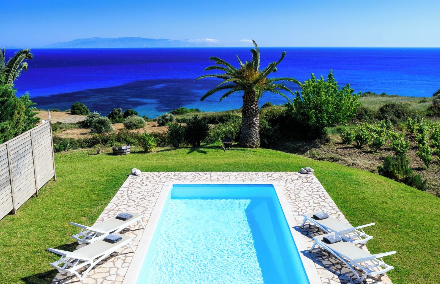 Una piscina rectangular con borde de piedra, rodeada por un césped con sillas de descanso.