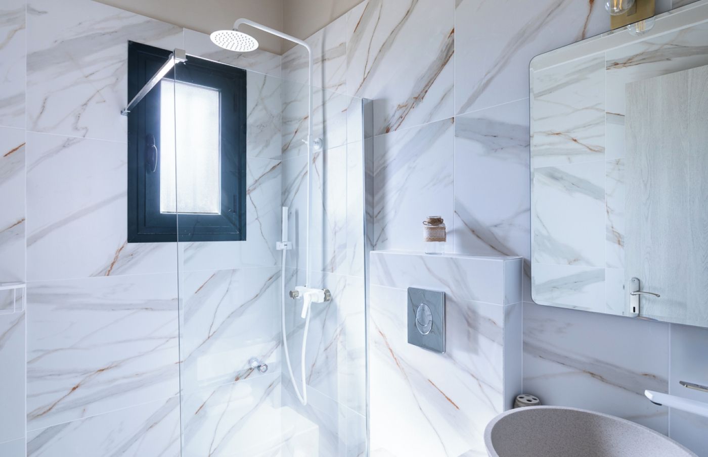 Ein modernes Badezimmer mit einer gläsernen Duschkabine, Marmorwand und integriertem Waschtisch.