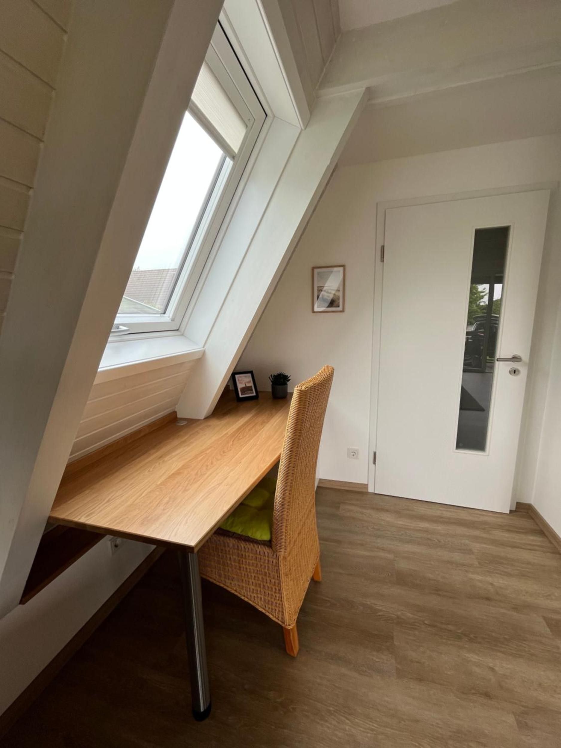 Et værelse med skrå vægge, et vindue, en dør og et bord med en stol.