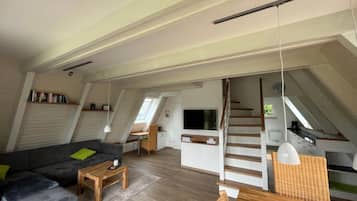 A spacious loft with a high ceiling, a staircase, a flat-screen TV, and a dining area.