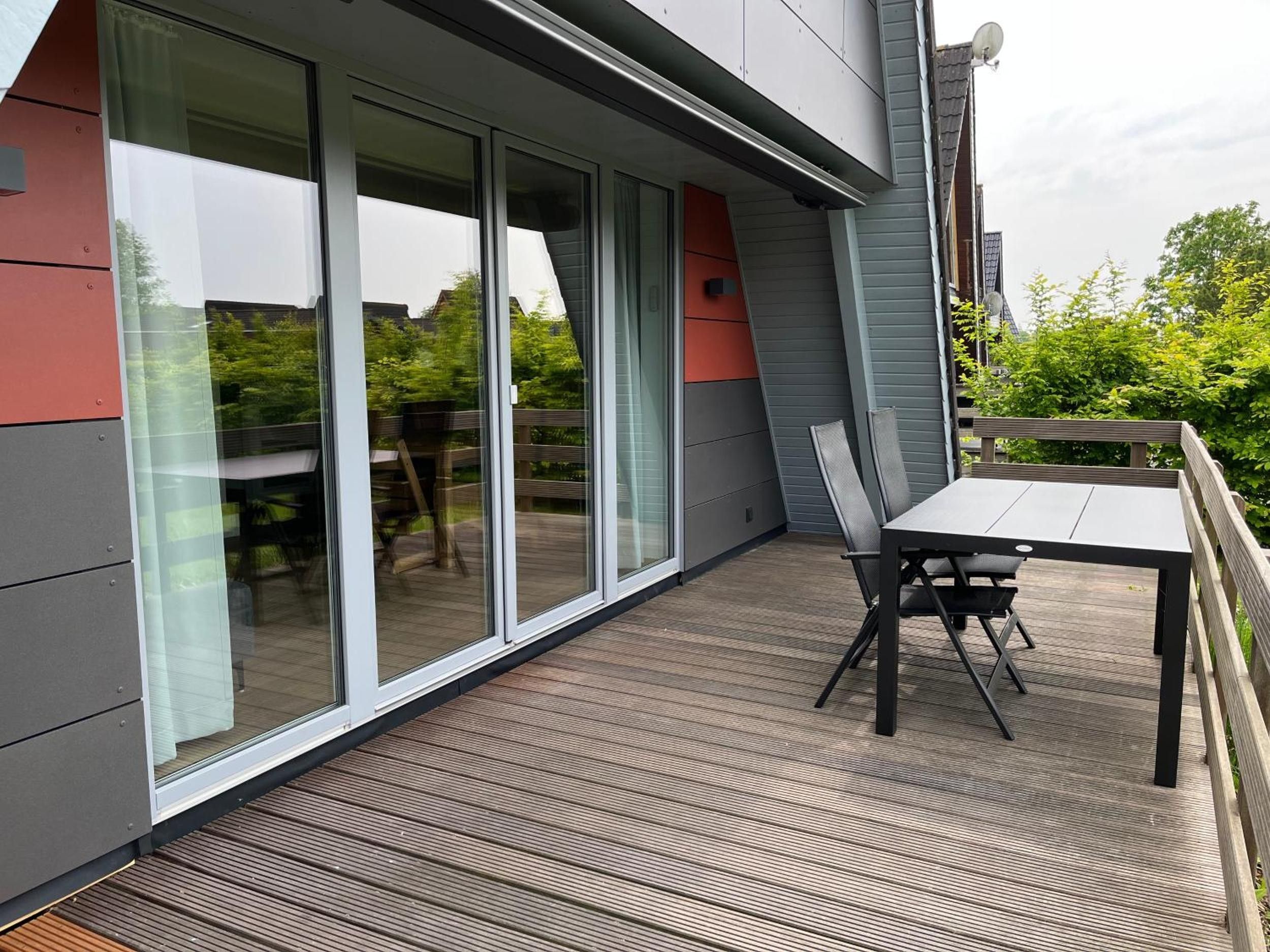 Eine moderne Außenterrasse mit Tisch und Stühlen, großen Schiebeglastüren und Blick ins Grüne.