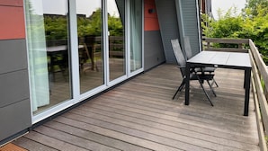 Una terrazza esterna moderna con tavolo e sedie, ampie porte scorrevoli in vetro e vista sul verde.