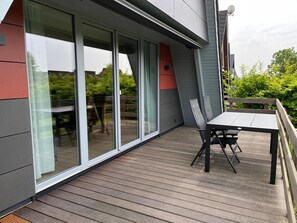 Eine moderne Außenterrasse mit Tisch und Stühlen, großen Schiebeglastüren und Blick ins Grüne.