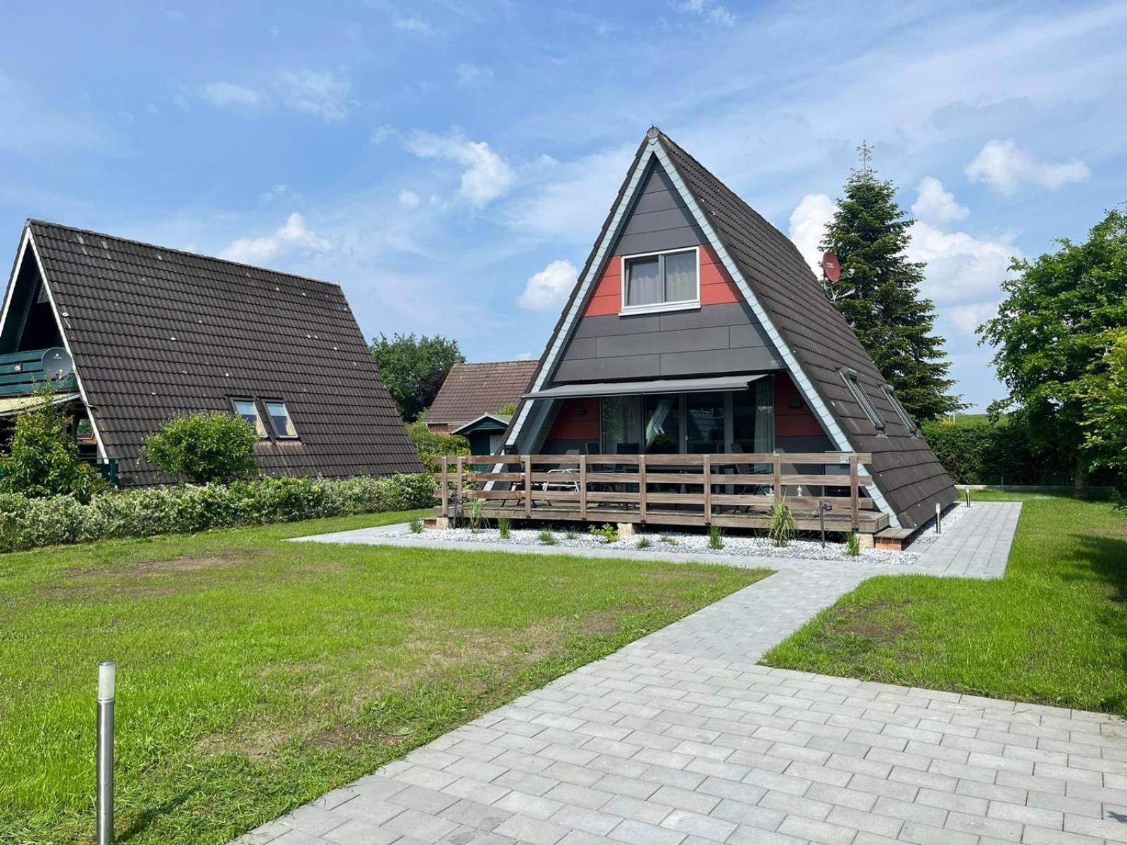 Ein modernes Haus mit geneigtem Dach, einer Holzterrasse und einem gepflasterten Weg zum Eingang.