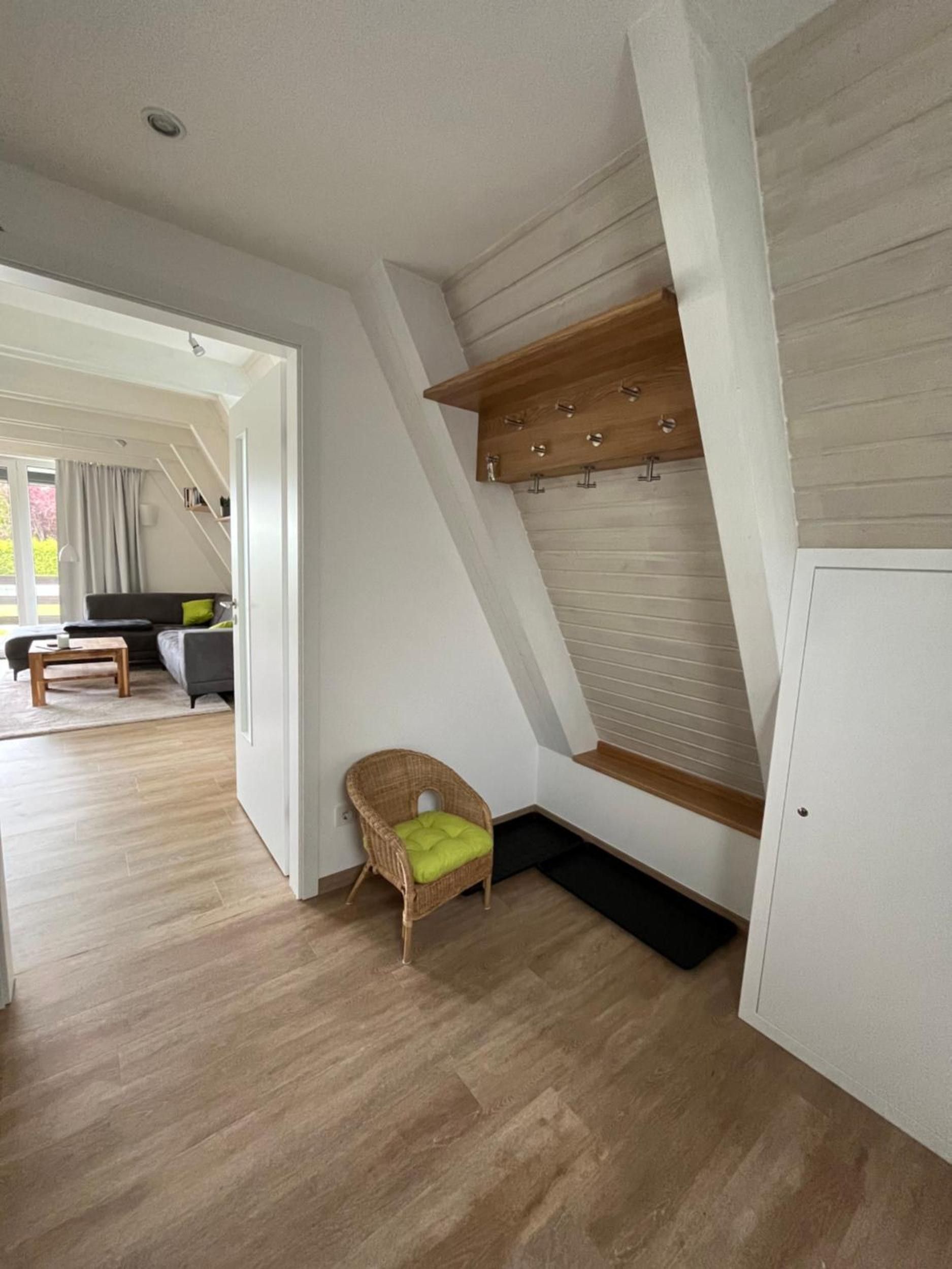 Ein Zimmer mit schrägem Dach, ein Korbstuhl mit Kissen, ein Holzregal mit Haken und eine weiße Tür.