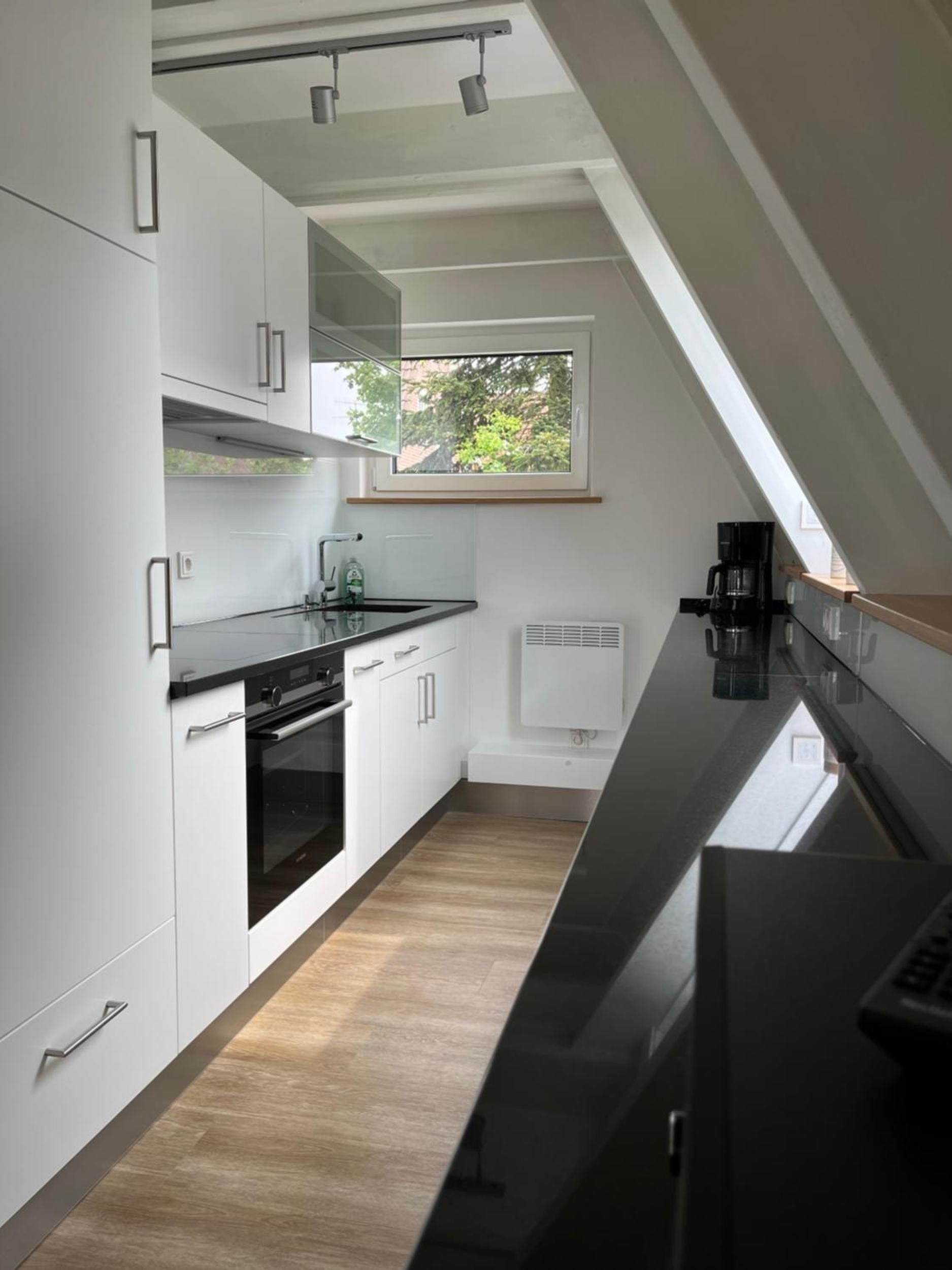 Eine moderne Küche mit weißen Schränken, einer schwarzen Arbeitsplatte und einem Fenster für natürliches Licht.