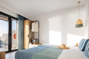 A modern bedroom with a large bed, a hanging light fixture, and a view of the outdoors. - Villa Near Agios Pavlos Beaches (Agios Vasileios)